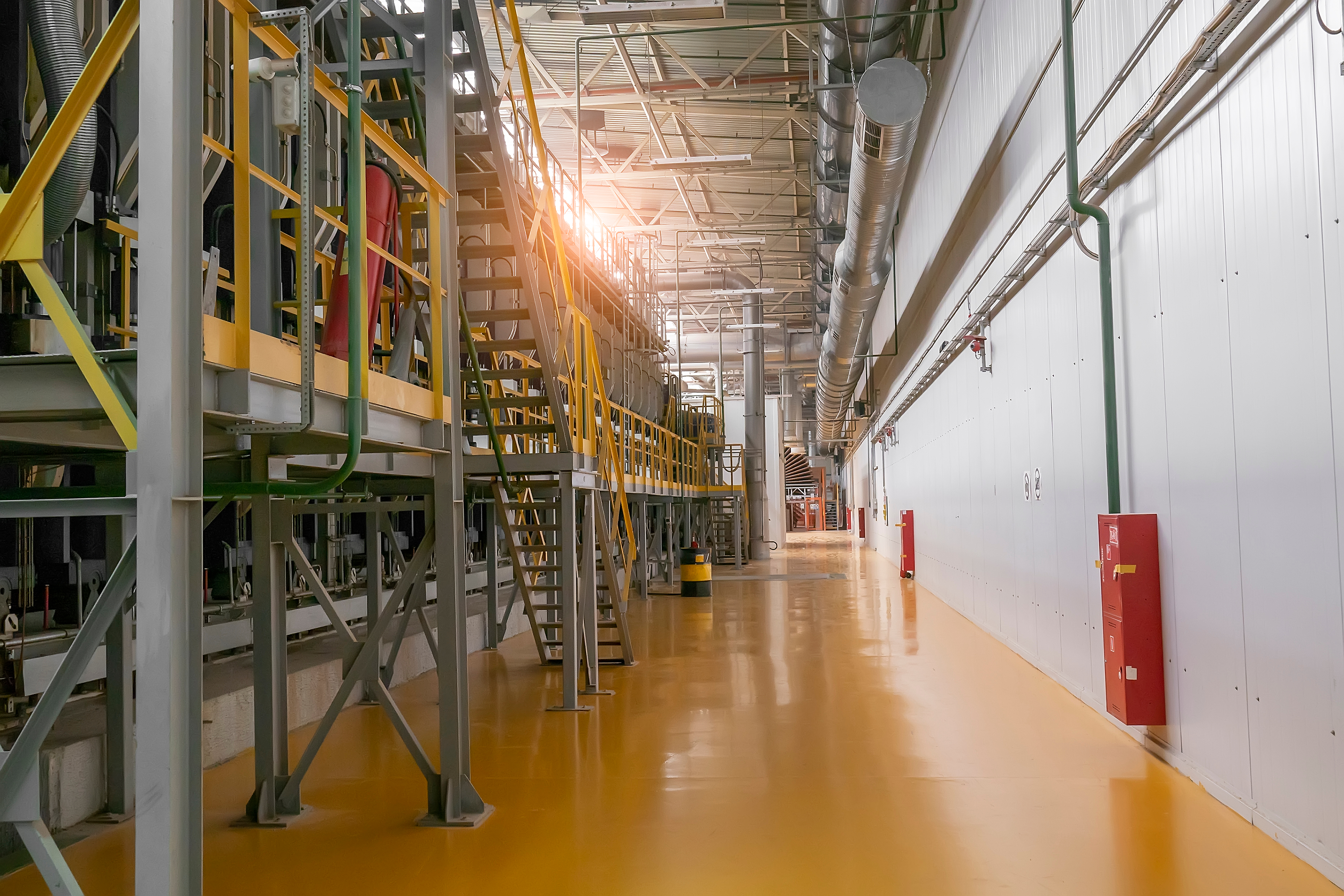Large industrial food manufacturing facility with a smooth orange polyurethane flooring surface, steel walkways, and ventilation ducting running the length of the production hall.